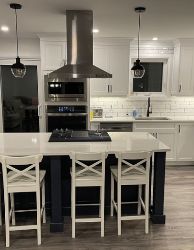 newly renovated kitchen featuring centre island with four white stools, a statement range hood, and gleaming white cabinetry